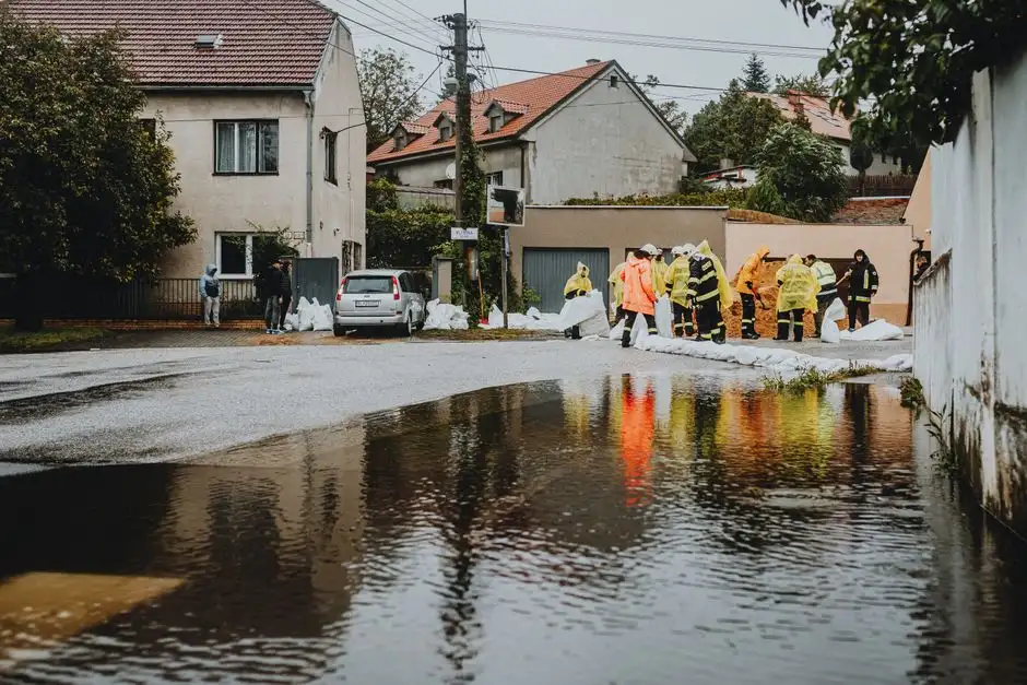 Emergency workers in rain gear manage floodwaters in a suburban street.